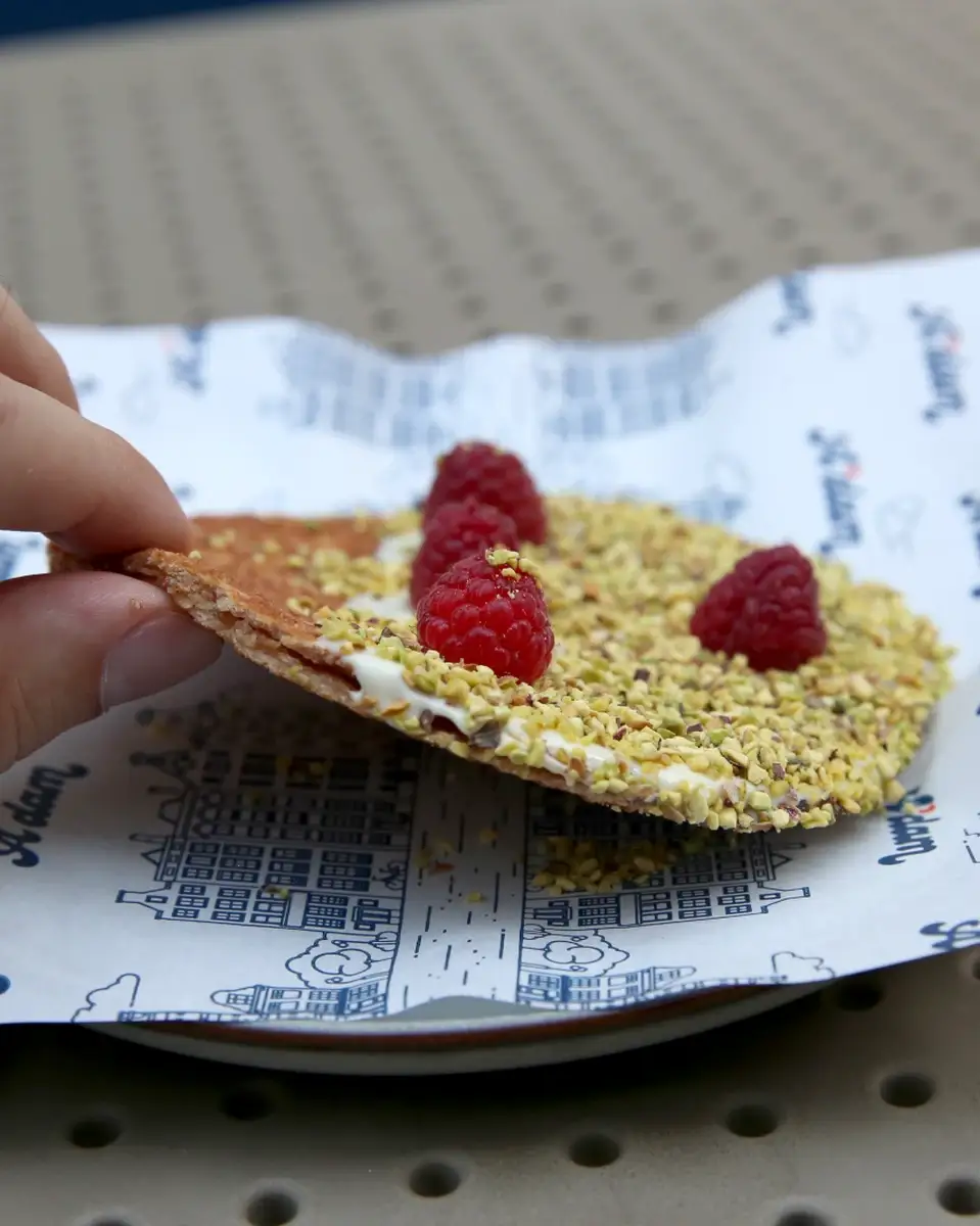 Ruka drži parče stroopwafela sa malinom i pistaćima, A'dam Stroopwafel Beograd