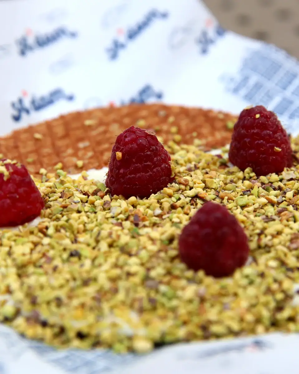Krupni plan svežih malina i seckanih pistaća na stroopwafelu, A'dam Stroopwafel